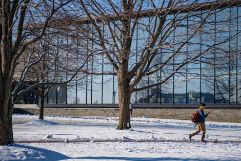 A student walks in front of Skillman LIbrary, surrounded by snow.