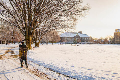 A person walks on a snowy path in front of the Quad, surrounded by snow.