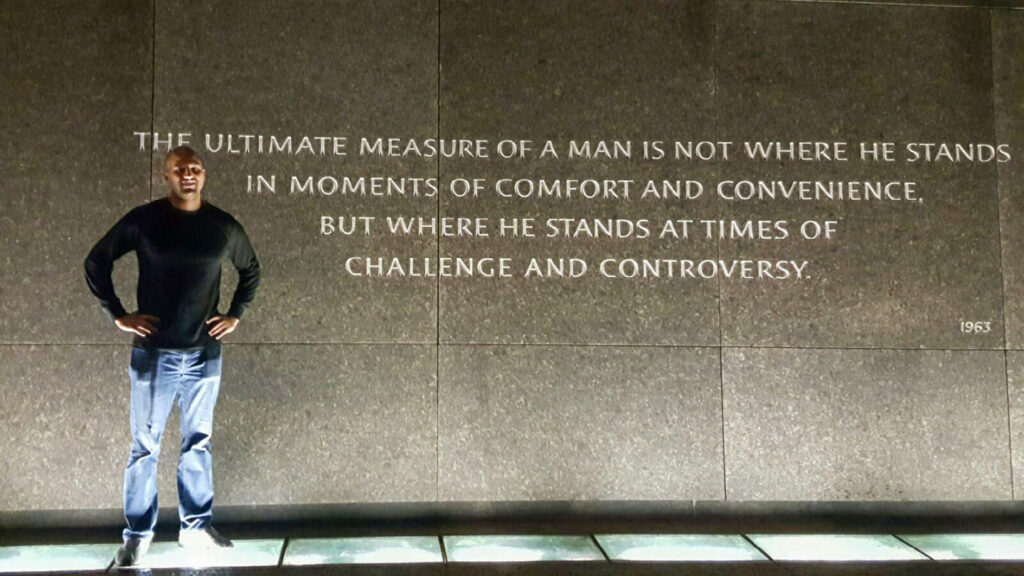 Yusuf Dahl stands in front of the quote: ‘The ultimate measure of a man is not where he stands in moments of comfort and convenience, but where he stands at times of challenge and controversy.’