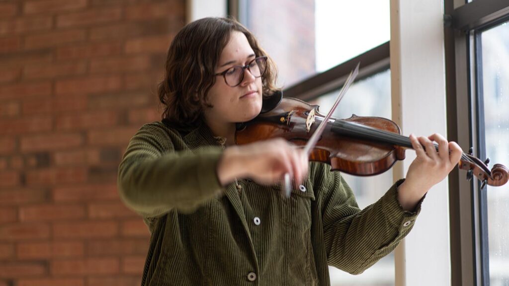 Student plays violin near window of Williams Center for the Arts