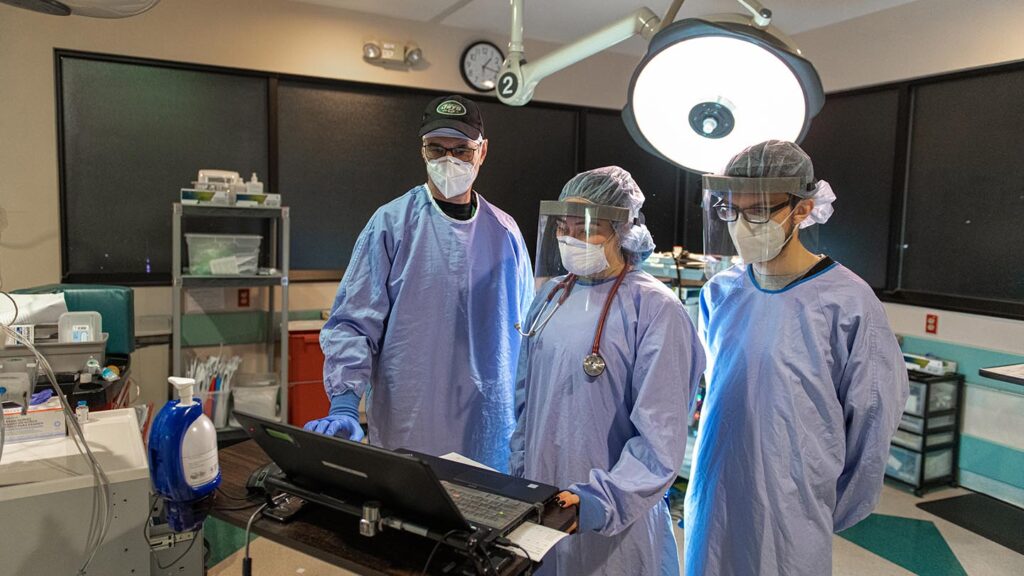 Doctor and students in blue scrubs look at computer in OR