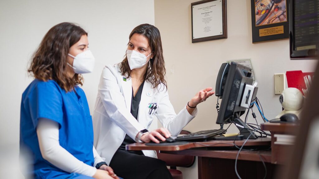 Doctor gestures to computer while talking to a student in a medical office