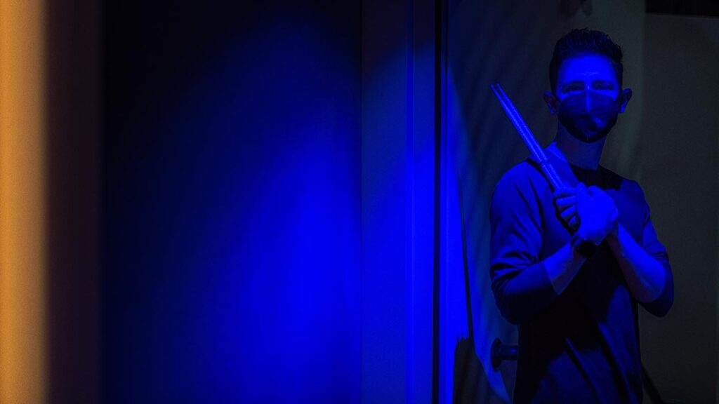 Bathed in blue light, student stands holding drum sticks