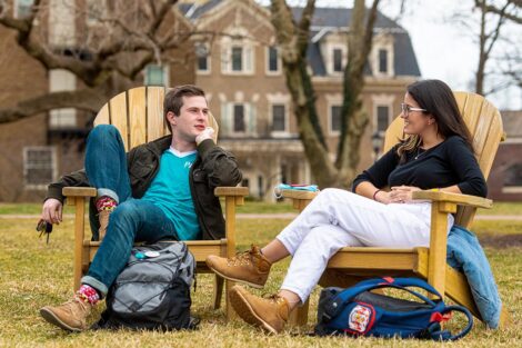two students sit in Adirondack chairs and talk on the Quad