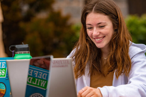 student smiles while working on laptop outside