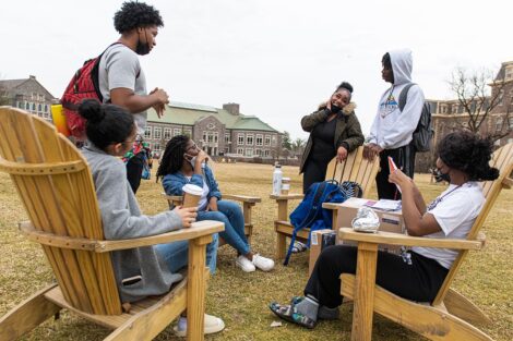 group of students sit in a circle in Adirondack chairs on the Quad