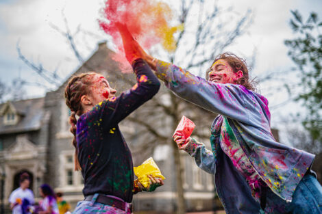 Two students high give with colorful powder.