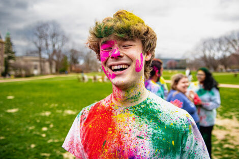 A student smiles, covered in colorful powder.