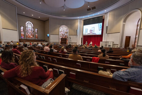 staff and faculty sit in Colton Chapel, Bob Sell on the screen above the stage