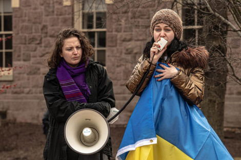 student holding a Ukrainian flag speaks into a microphone