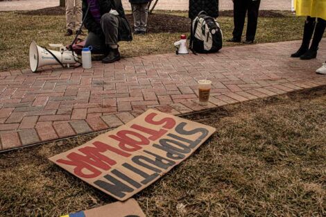 faculty member speaks into a microphone, signs supporting Ukraine lie on the grass on the Quad