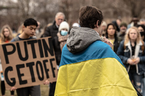 student draped in a Ukrainian flag speaks toward crowd of students on Quad