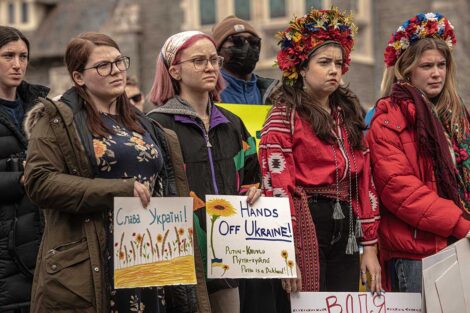 students gather with signs supporting Ukraine, two students dressed in traditional Ukrainian clothing and head accessories