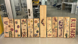 a series of wooden swing seats stand upright, each is decorated with writing and colorful drawings