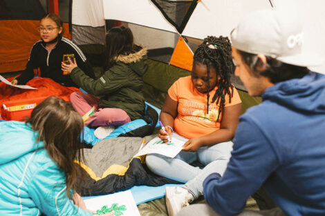 elementary school students sit in a tent and draw