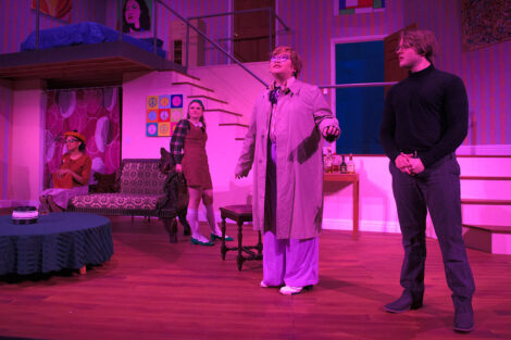 students in a stage production act on stage with pink dramatic lighting
