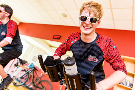student rides a spin bike and smiles wearing sunglasses