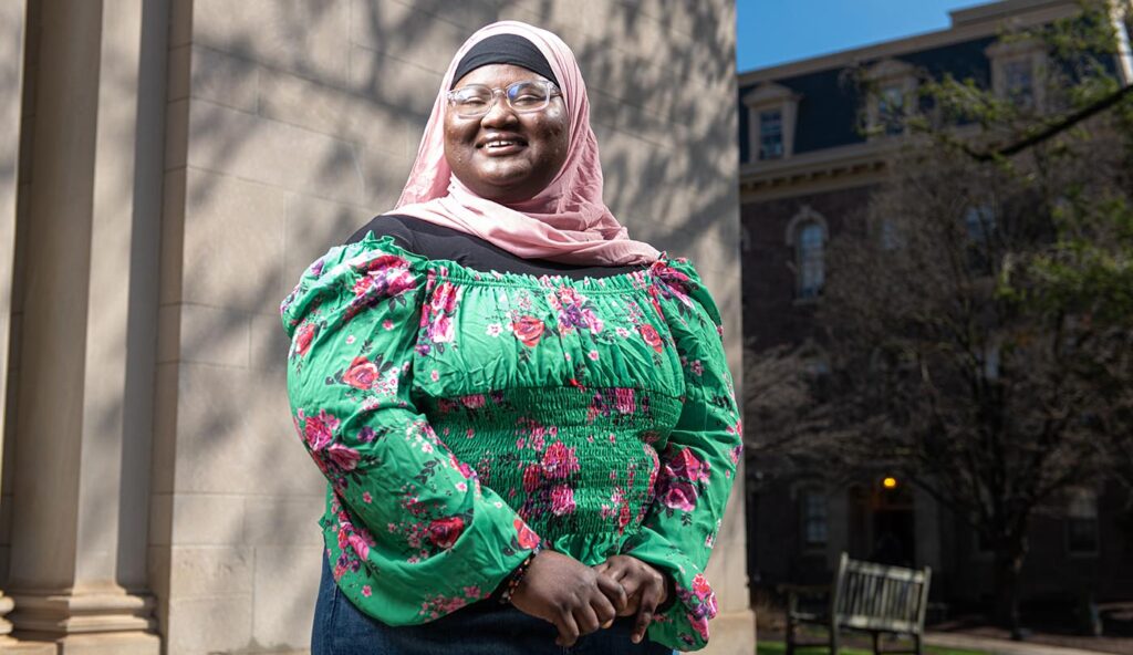 Fatimata Cham wears a pink headscarf and smiles in front of Colton Chapel