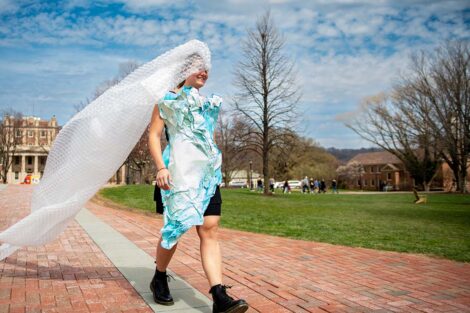 Student walks down sidewalk with white veil trailing in the breeze