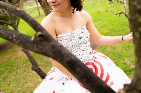 Student sits in a tree wearing a dress made of plastic bags