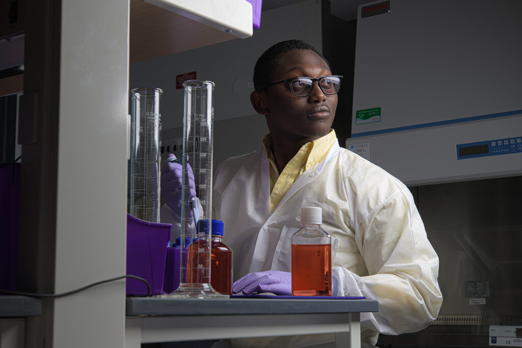 Kwabena Aceampong, wearing a lab coat and gloves, works in a lab of Rockwell Integrated Sciences Center.