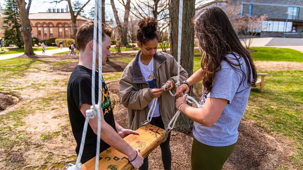 students tie knots in rope as they hang a swing from a tree