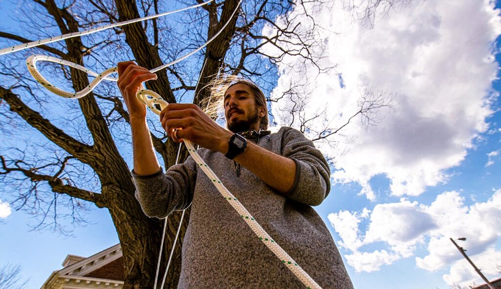 student ties a rope knot while hanging a swing from a tree
