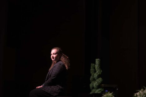 Performer sits alone on a bench on stage