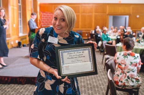 Prof. Lauren Anderson holds a framed award and smiles