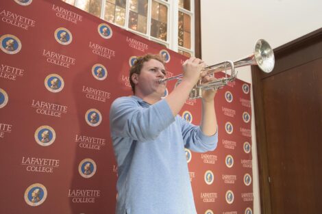 student plays the trumpet with a Lafayette College backdrop