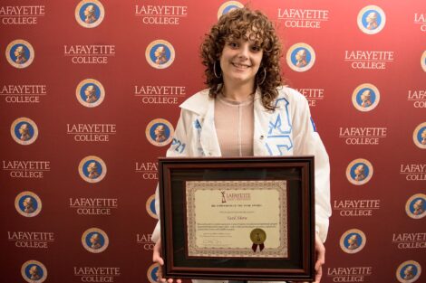 student holds an award against a Lafayette College backdrop