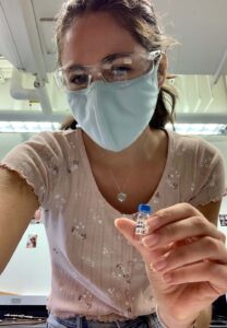 Camille Carthy wears a mask while holding a small vile in a lab