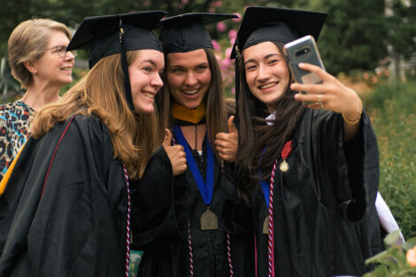 three grads in caps and gowns smile while one takes a selfie
