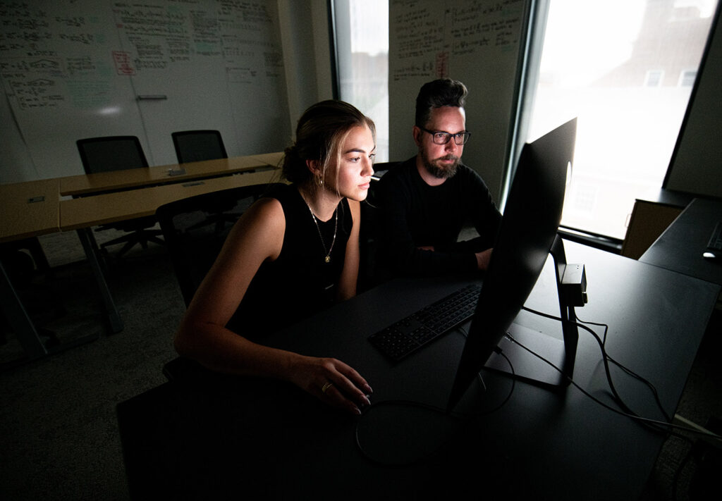 Daniel Strömbom and Grace Tulevech sit at a computer together, light shines on Grace's face