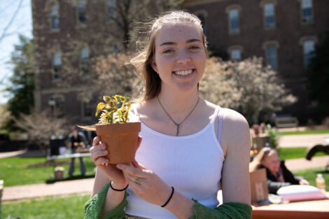 student smiles while holding a potted plant on the Quad