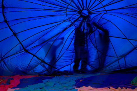 shadows of workers are visible through the blue fabric of the hot air balloon