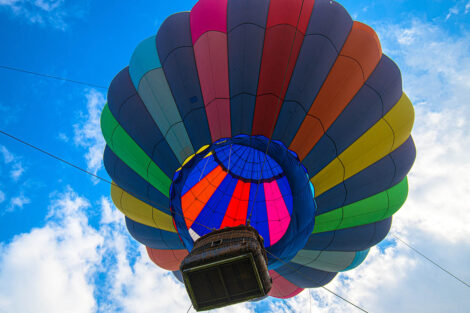looking up underneath the hot air balloon as it rises in the air with a bright blue sky