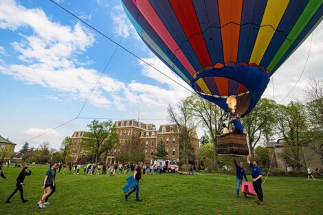 students gather on the Quad where the hot air balloon sits with a basket