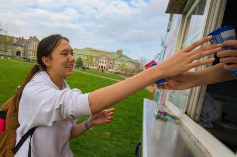 student smiles while reaching for ice cream from ice cream truck on Quad