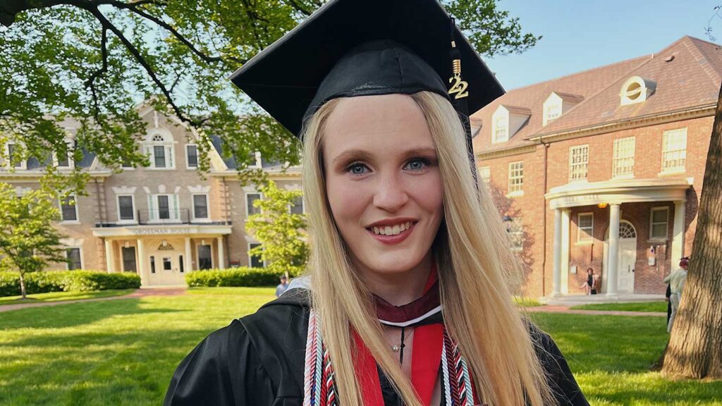 Class of 2022 valedictorian Jillian Updegraff wearing graduation cap and gown, standing outdoors in front of Lafayette College's Grossman House