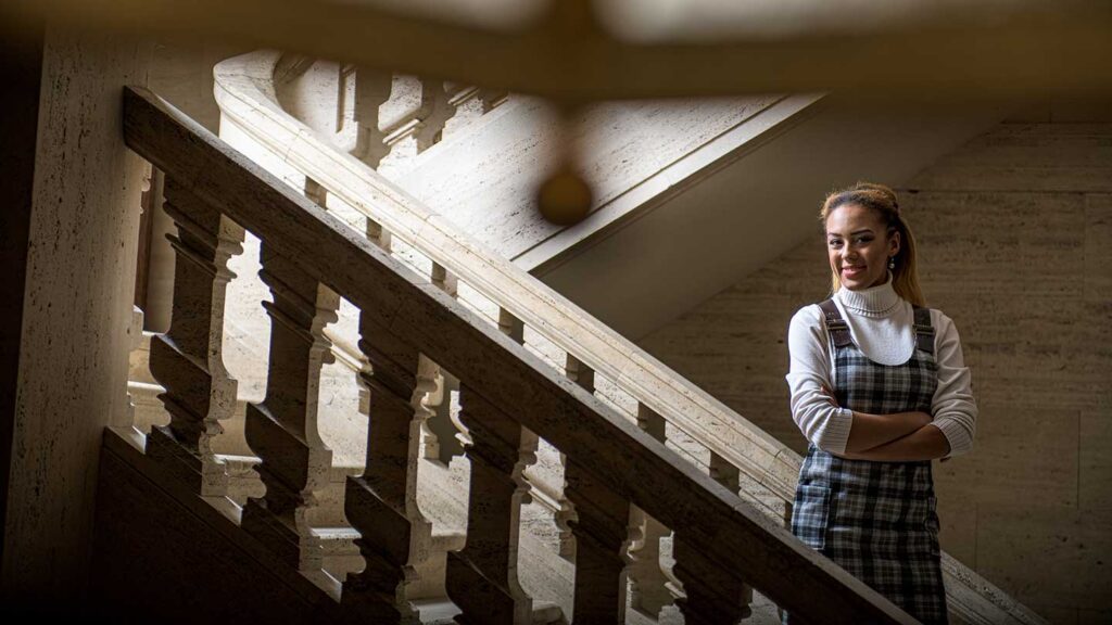 Class of 2022 valedictorian Kelly Mwaamba standing on a marble staircase