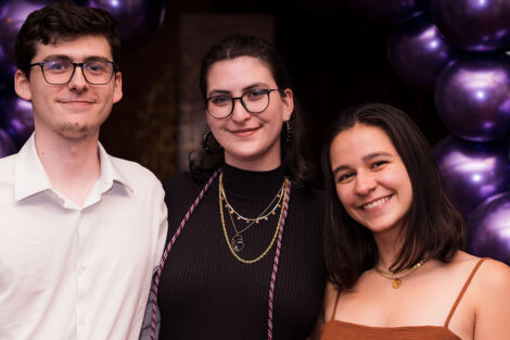 three students in front of purple balloon arch
