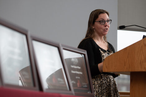 Chelsea Morrese stands at a podium and talks, to her left is a table with awards