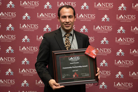 community member holds an award in front of a Landis backdrop