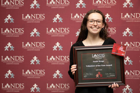 student holds a Landis award in front of a Landis backdrop
