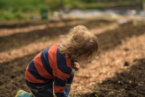 a young child sits in a dirt garden bed