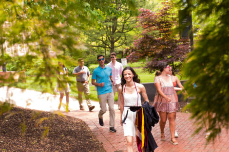 Students walk on a brick path, holding cap and gown.