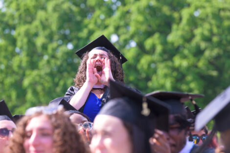 A graduate stands up in the crowd, screaming in celebration