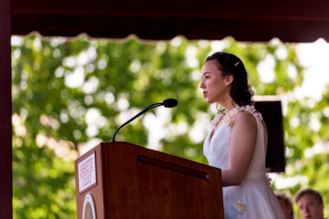 student in white dress stands at podium