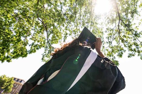 sun shines through trees and illuminates student in cap and gown